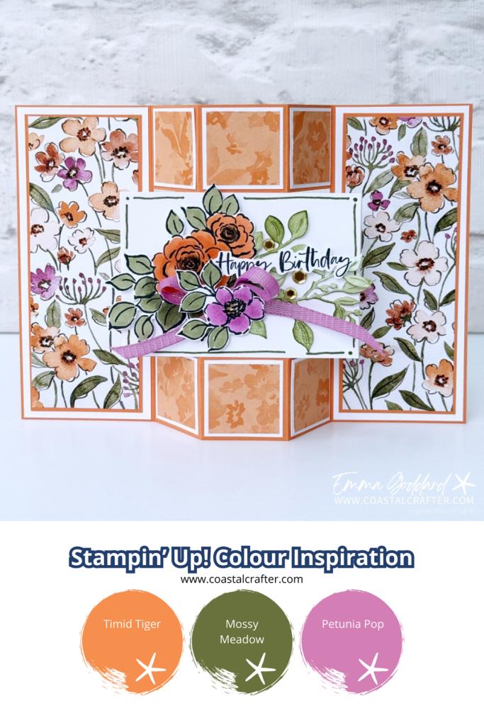 A handmade floral birthday card with a unique gatefold design. The card features panels decorated with watercolour orange, purple, and white flowers on a white background. The centre panel displays a cluster of coloured flowers in orange and purple, accented with green leaves, a purple ribbon, and a "Happy Birthday" sentiment in elegant script. The card has a dimensional, layered look and is framed in timid tiger cardstock. The creator's watermark, "Emma Goddard | www.coastalcrafter.com," is visible in the bottom right corner.