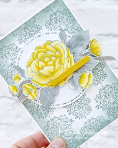 Handmade card featuring a large Daffodil Delight rose with Smoky Slate leaves coloured with Stampin' Blends, made using the Sweetly Sentimental and Echoes of Details focus products. The rose sits on a white stitched circle die cut over a Smoky Slate damask patterned background, with Grey Granite linen ribbon and a Crushed Curry sentiment strip reading 'have a lovely day', hot foiled."